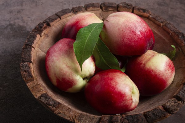 Ripe nectarine, in a wooden plate, brown background, top view, no people