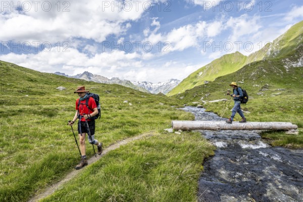 Two mountaineers crossing a stream on a tree trunk, mountain landscape with mountain stream,