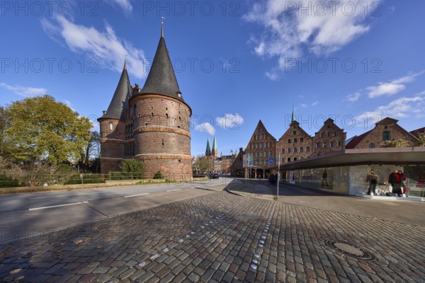 Lübeck Holstentor, side view, pedestrian crossing, cobblestone pavement, blue sky with fair weather