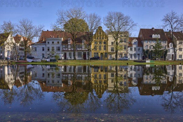 Historic houses, symmetrical reflections on the water surface, river Trave, cloudless blue sky, old