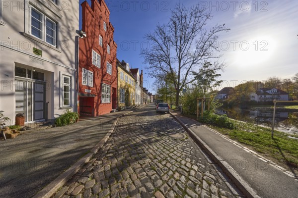 Historic houses, cobblestone pavement, bare trees, river Trave, backlight of the sun, street, old