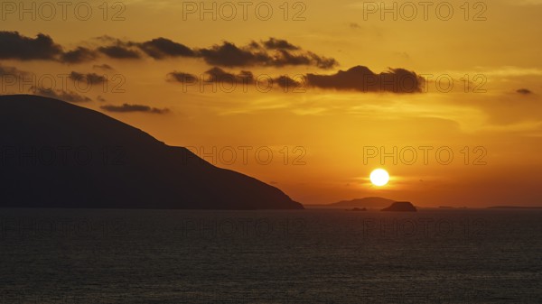 Still life of a sunset over the sea with mountains on the horizon and a sky in yellow and orange,