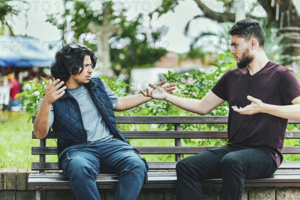 Two people arguing on a park bench. Two guys arguing sitting on a bench