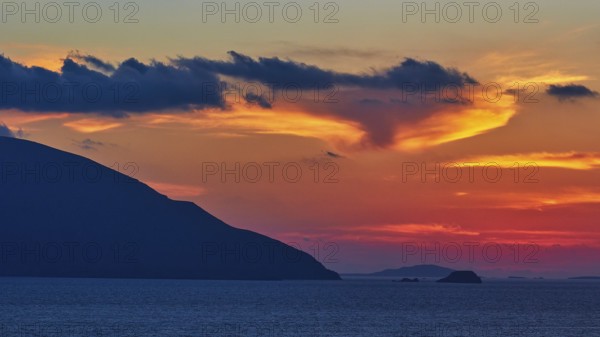 Play of colours in the evening sky over the sea, hills as silhouettes in front of a colourful