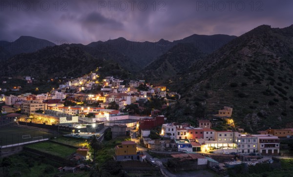 View of Vallehermoso and the surrounding mountain landscape at dusk under a cloudy sky. The street