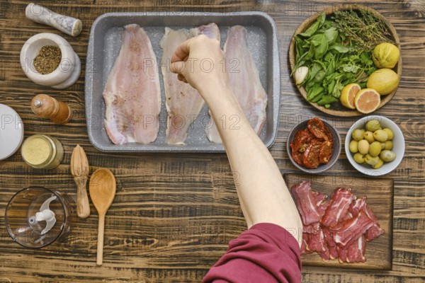 Sliced fish is placed in a baking tray while an outstretched hand sprinkles seasonings over it.
