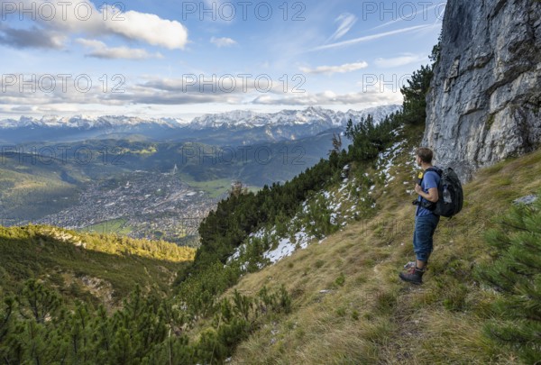 Mountaineer on a narrow hiking trail between mountain pines, view of Garmisch-Partenkirchen and