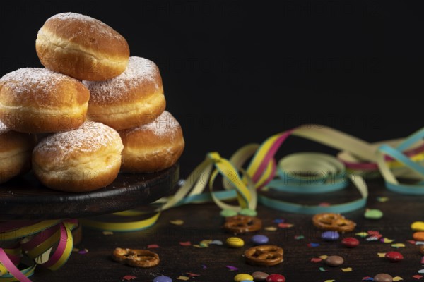 Berliners, doughnuts with icing sugar are piled up against a dark background next to confetti and