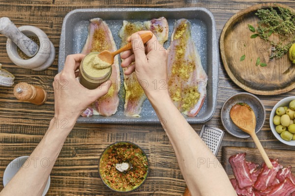 A person is mixing a spice blend in a jar while seasoning fish fillets laid out on a baking tray