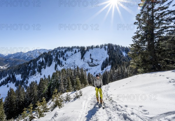 Ski tourer in wintry mountain landscape with sun star, ascent to Roßkopf, Mangfallgebirge, Bavaria,