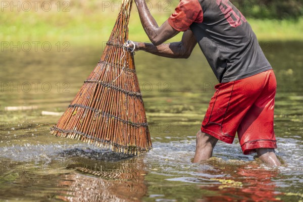 Fisherman lifting the basket out of the water. Water trips down the basket. He uses the basket for