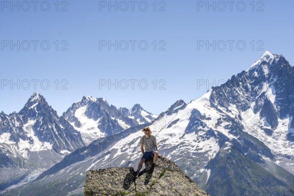 Mountaineer sitting on a rock and looking into the camera, mountain landscape with mountain peak