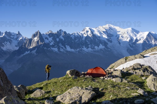 Photographer with telephoto lens next to red tent, mountain landscape in the morning light,