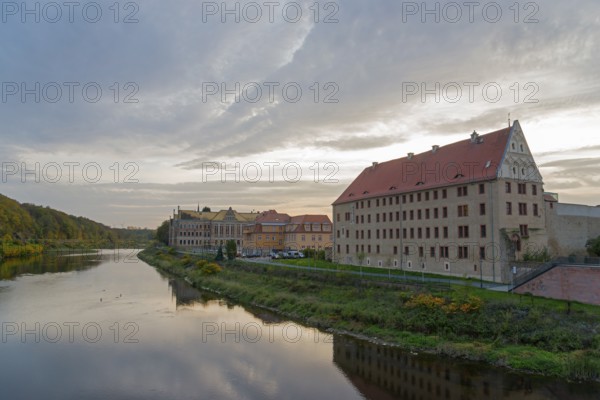 River landscape with buildings along the bank at dusk and reflection in the water, River Mulde,