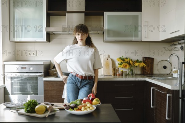 Woman stands in a stylish kitchen surrounded by fresh fruits and vegetables on the table