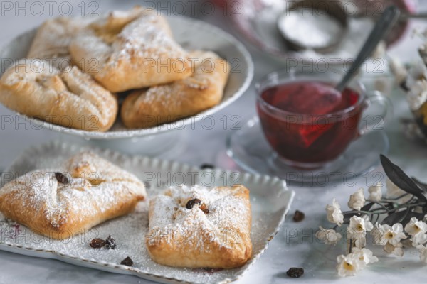 Delicious puff pastries, curd cheese golaches with icing sugar next to a cup of tea and decorative