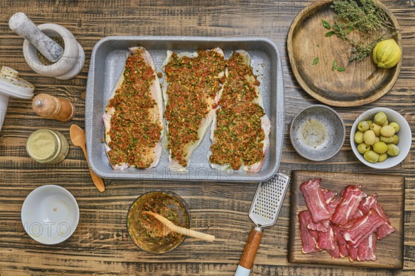 Three fish fillets are seasoned with herbs and spices, surrounded by a variety of ingredients on a