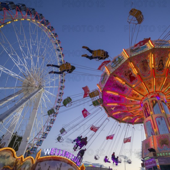 A funfair at dusk with illuminated chain carousel and Ferris wheel, Europa Rad, rides, wave flight,