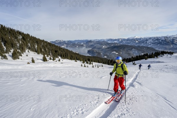 Ski tourers ascending Simetsberg, view of Walchensee and mountain panorama, Estergebirge, Bavarian