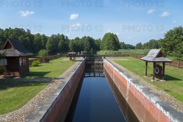 A narrow canal with a lock leads through a green forest landscape, Tartak Lock, Augustow Canal,