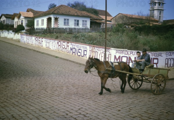 Man and boy riding on a horse-drawn cart past election campaign posters of politician João Mansur