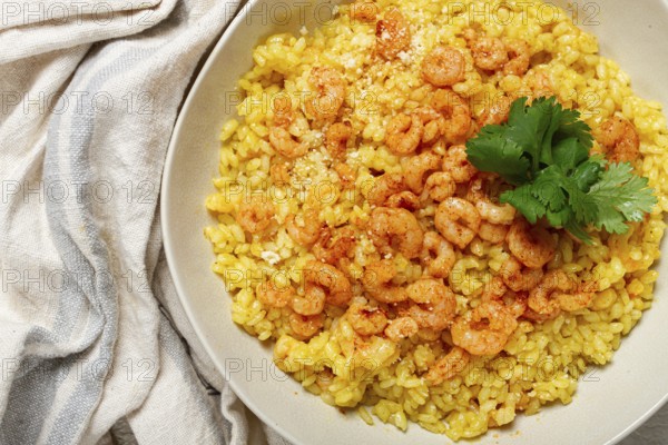 Risotto with shrimp, in a bowl, on a textured surface, with a side dish of fresh coriander,
