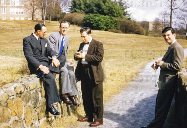 Four elegantly dressed men in business suits outdoors, USA around 1953, standing, sitting against