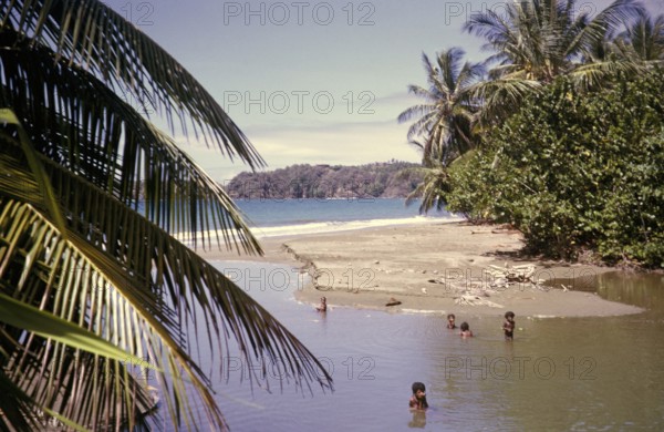 Local children swimming by beach in tidal river at the coast, island of Tobago, 1963