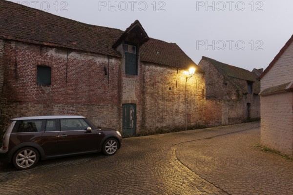 Modern Mini Clubman parked in an old village alleyway with brick buildings, twilight, Damme, West