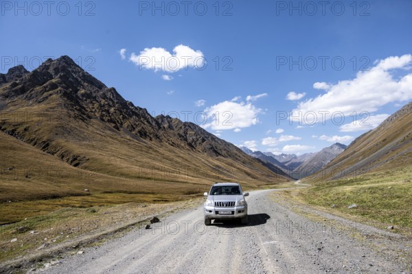 Off-road vehicle driving on a gravel track in a valley, picturesque mountain landscape with white