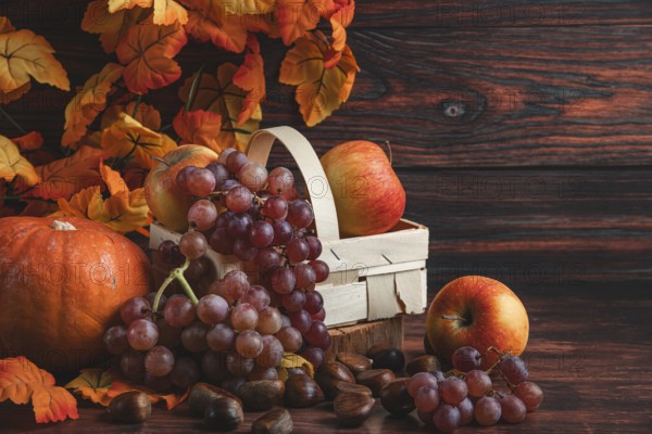 A wooden basket with apples and grapes next to chestnuts, a pumpkin and autumn leaves