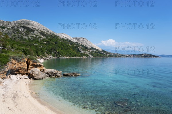 Clear blue sea water on a sandy beach with rocky coastline under a cloudless sky, bay near Stara