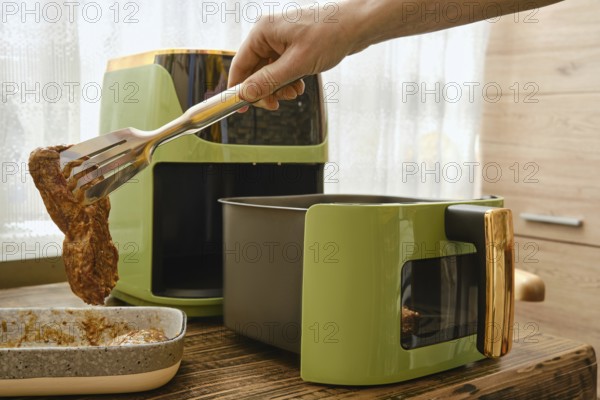 A hand lifts a piece of marinated meat and place it an air fryer, showcasing the cooking process.