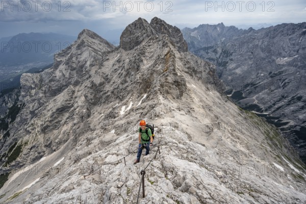 Mountaineer with helmet climbing in a secured climb on the rock, on a narrow rocky ridge, crossing