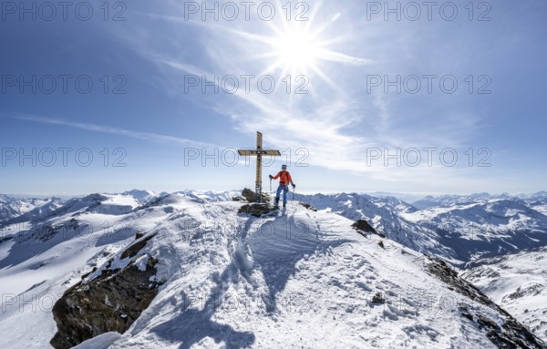 Ski tourer at the summit of Monte Cevedale with summit cross, sun star, mountain panorama,