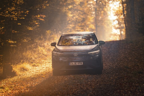 Car driving on a forest path covered with leaves on a sunny autumn day, electric car VW ID5,