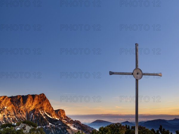 Sunrise at the summit cross of the Rauhen Kopf, behind the Untersberg, Berchtesgaden Alps,