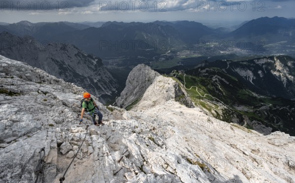 Mountaineer with helmet climbing on the rock in a secured climb, on a narrow rocky ridge, in steep
