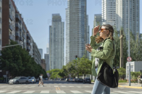 Young businesswoman crossing the street holding a coffee and protecting herself from the sun in