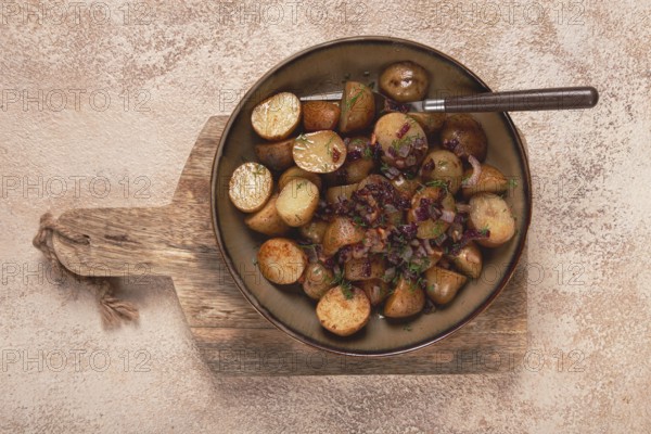 A bowl of golden roasted baby potatoes is garnished with herbs and garlic. It rests on a wooden
