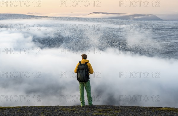 Young man in front of impressive landscape at sunset, fog, clouds moving around, glacier ice of the