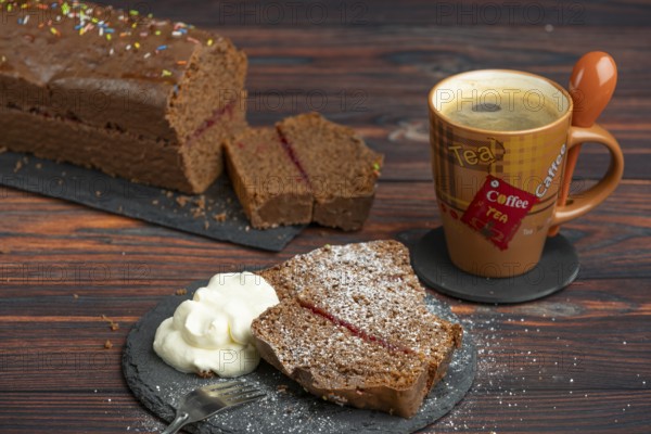 Chocolate cake, pieces with icing sugar and whipped cream, next to a cup of coffee