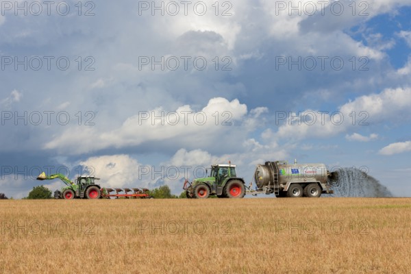 Two tractors in a field with a fertiliser spreader under a cloudy sky, Baden-Württemberg, Germany,