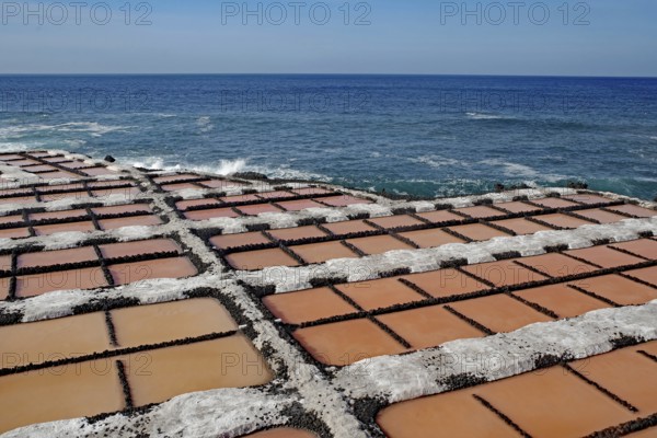 Regular arrangement of salt fields in orange near the blue sea under a clear sky, salt flats,