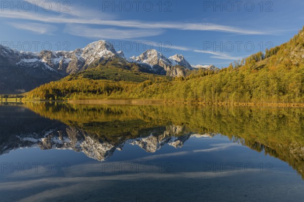 Lake Almsee in autumn with mountains reflected in the lake. Blue sky