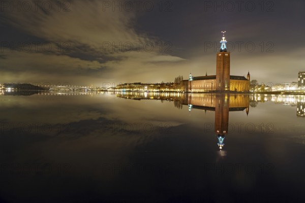 Night shot of an illuminated city building on the shore with reflection in the water, winter, ice,