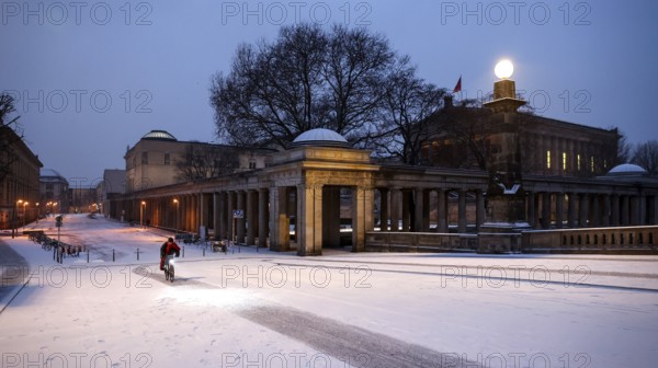 A cyclist rides over snow-covered streets at the old National Gallery in the early morning, Berlin,