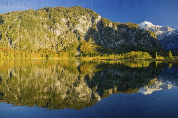 Lake Almsee in autumn with mountains reflected in the lake. Blue sky with no clouds