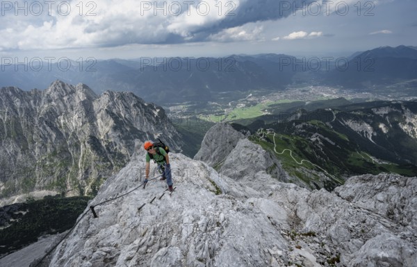 Mountaineer with helmet climbing on the rock in a secured climb, on a narrow rocky ridge, in steep