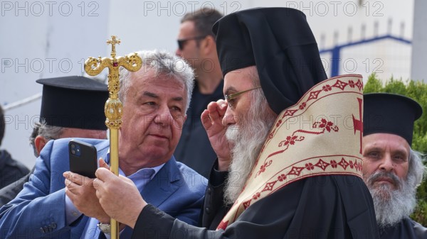 Archbishop Amphilochios, priest in religious dress looks at a smartphone during an outdoor